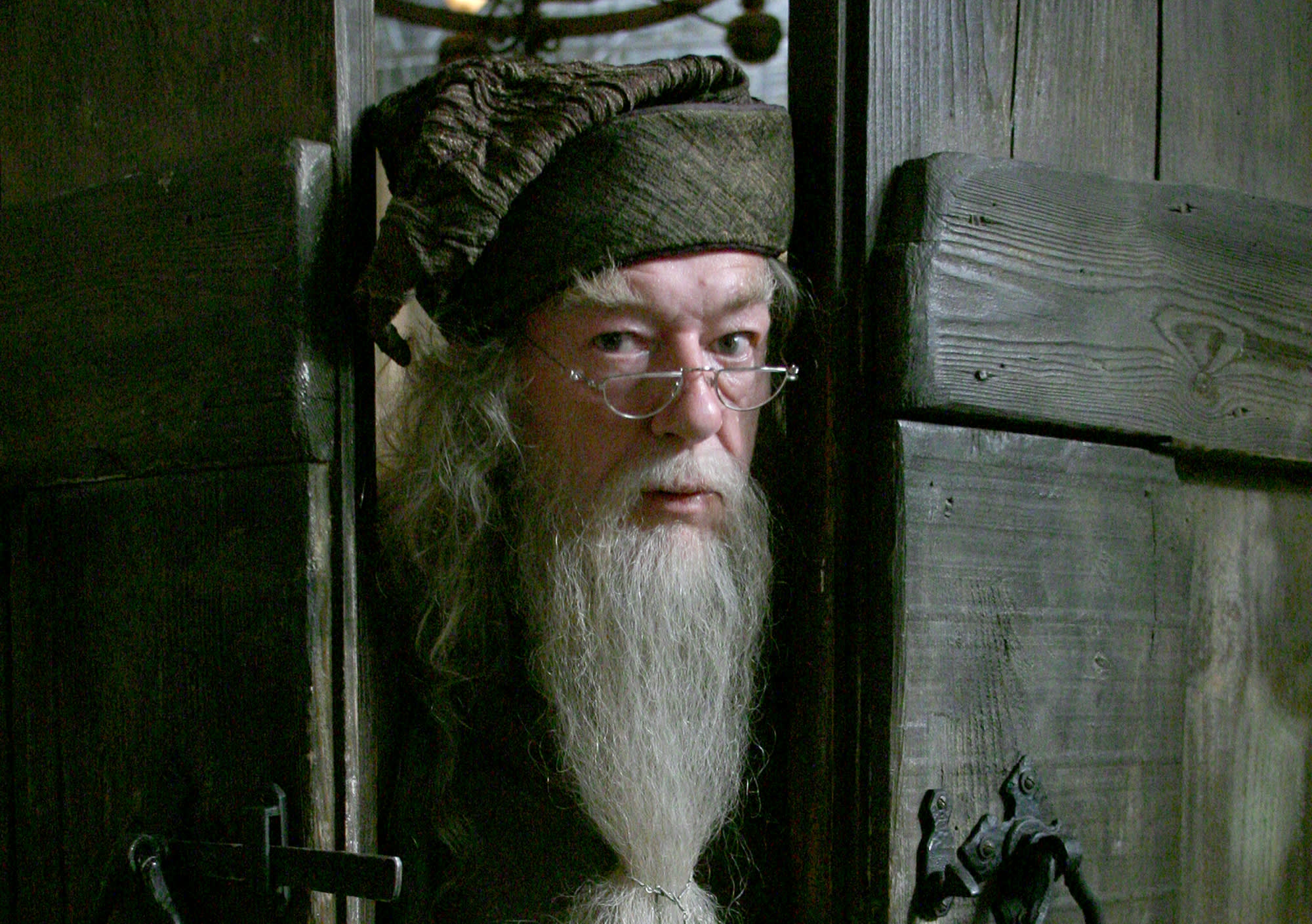 Albus Dumbledore is poking his head through the gap between a set of wooden doors.