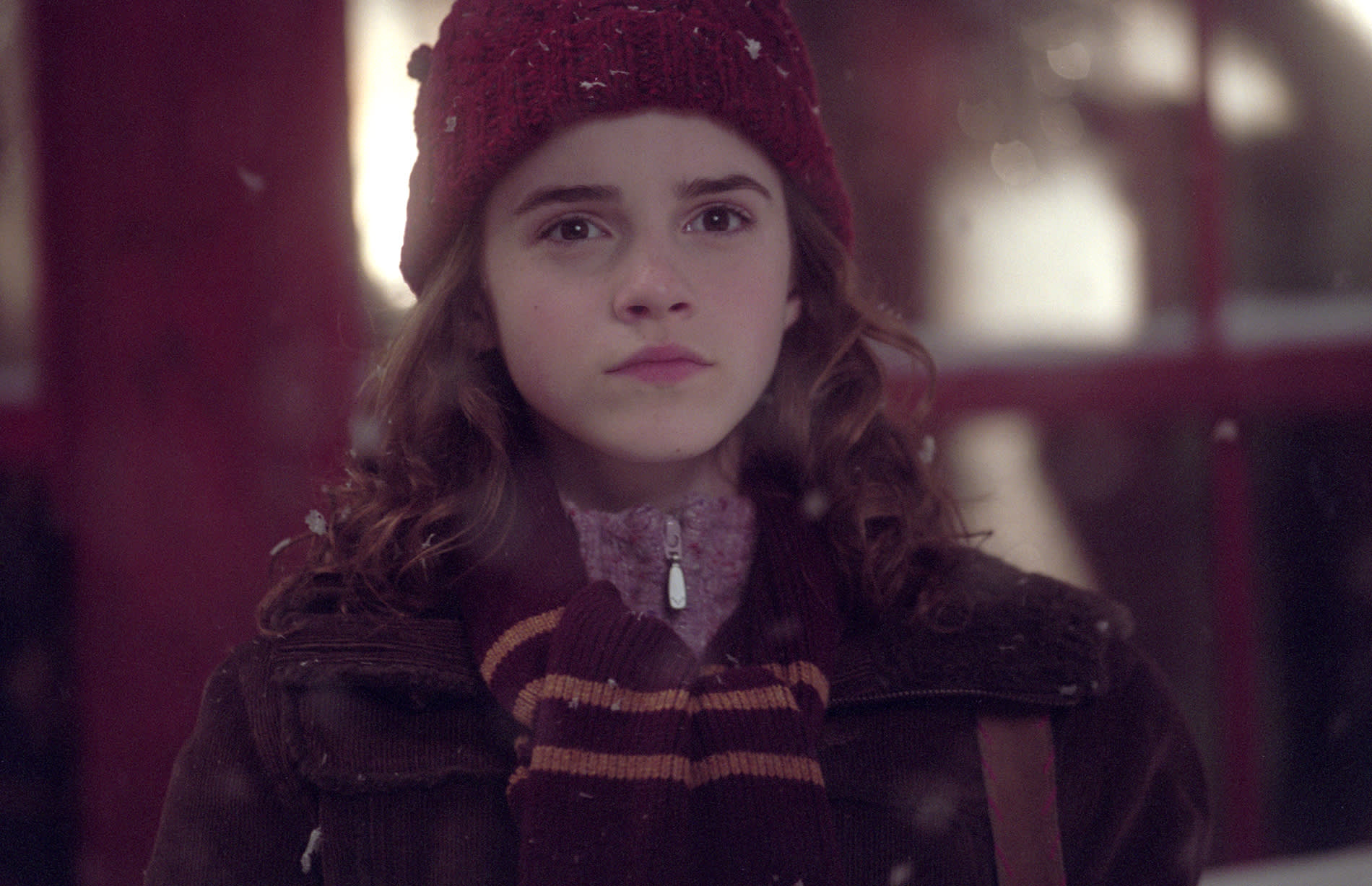 Hermione standing in the snow, wrapped up warm in a hat and scarf.