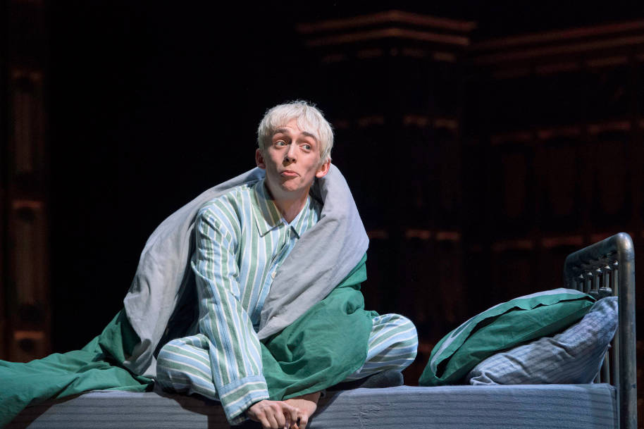Scorpius Malfoy is sat on his bed in his pyjamas. He has his duvet wrapped round him and is pulling a funny face.