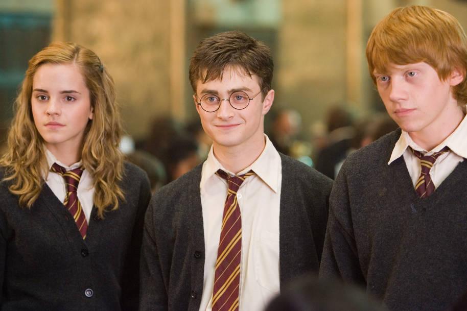 Hermione, Harry and Ron stand shoulder to shoulder in that order. Harry is smiling and they are wearing their Hogwarts school uniforms.
