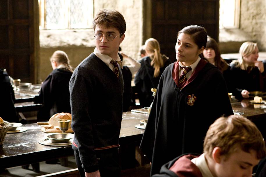 Harry Potter and Katie Bell are standing in the Great Hall and talking. Harry is looking over his shoulder.