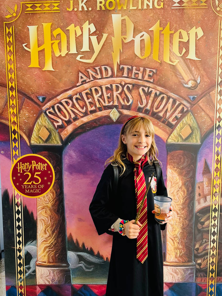 A girl wearing Gryffindor robes holding a Butterbeer and wand