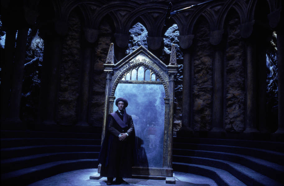 Professor Quirrell is standing with his back to the Mirror of Erised in a stone room.