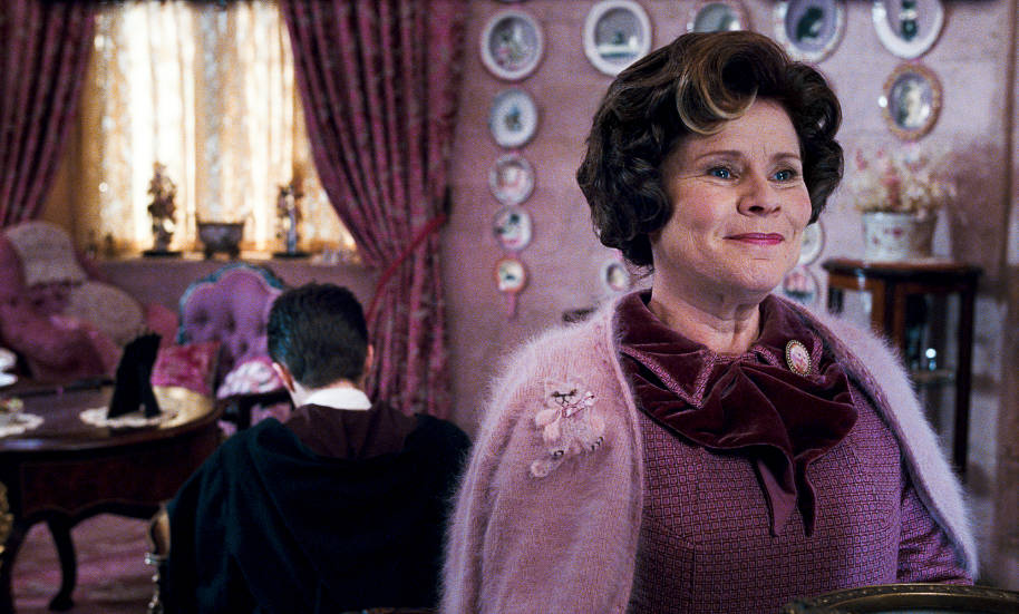 Harry is serving detention in Umbridge's office. She has her back to him and is smiling smugly.