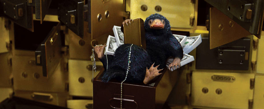 Newt's Niffler lying in a drawer while stuffing treasure into his pouch at the bank