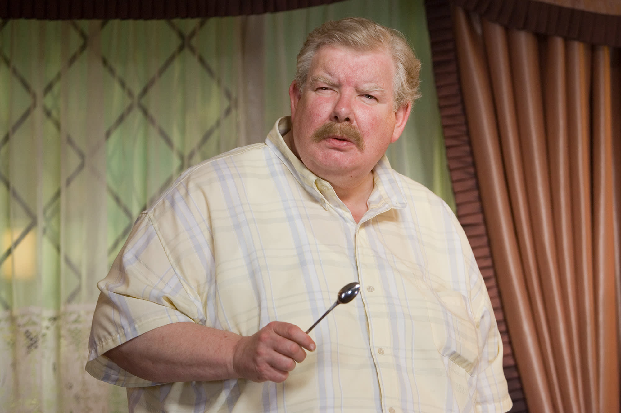 Vernon Dursley stood in the living room of Privet Drive holding a spoon and looking confused.