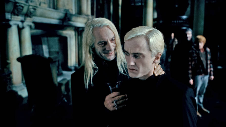 Lucius sourit à Draco et appuie affectueusement sur sa nuque pour persuader Draco d'identifier Harry Potter.