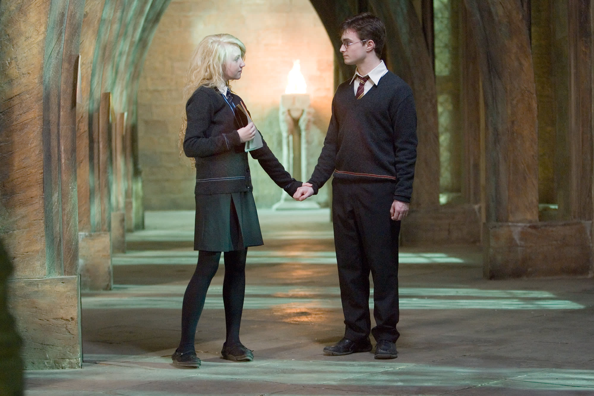 Harry and Luna standing in a corridor, looking at each other and holding hands.