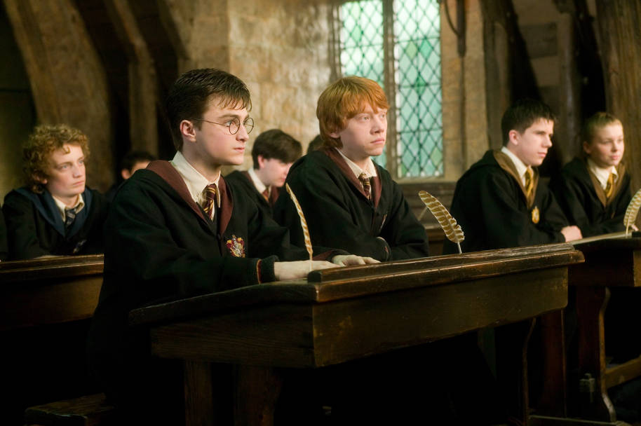 Harry and Ron next to each other at their desk in a lesson. Both are facing forward and listening.