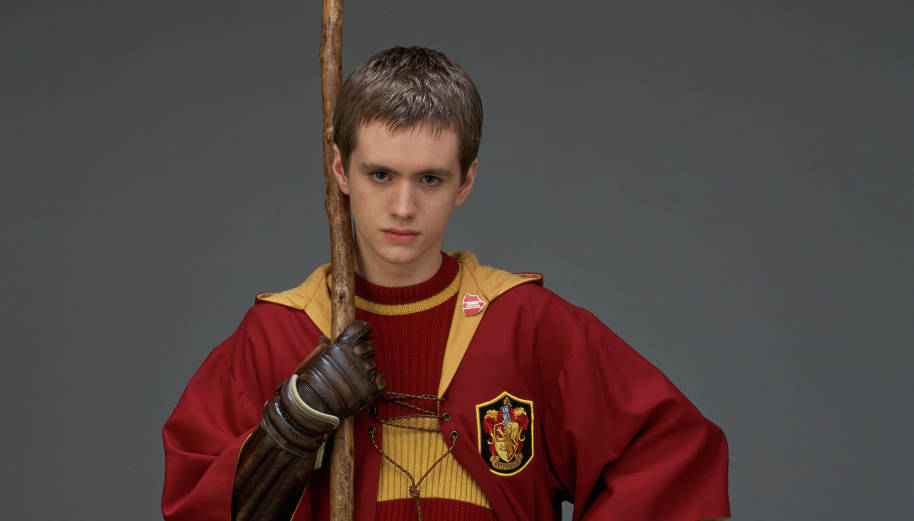 A close up of Oliver Wood who is wearing Quidditch robes and holding a broomstick.