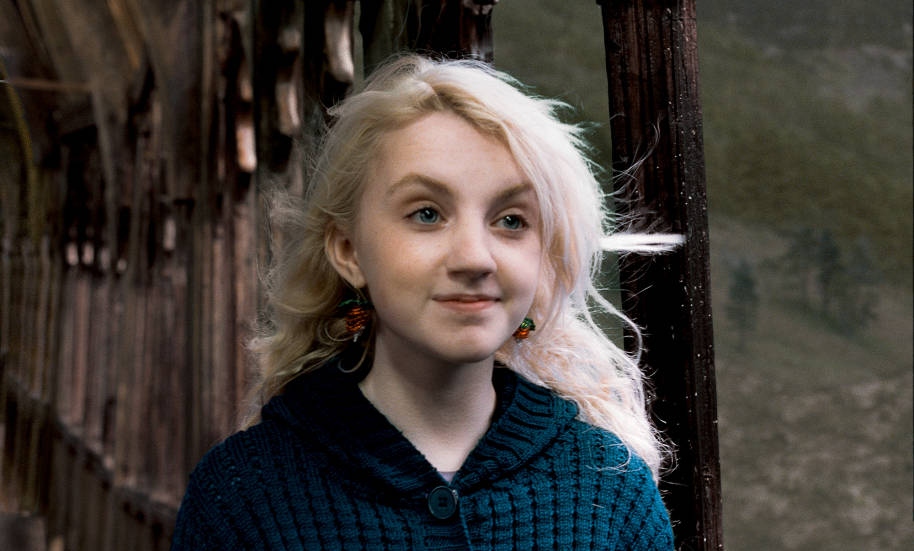 A closeup of Luna Lovegood standing on the bridge at Hogwarts and smiling