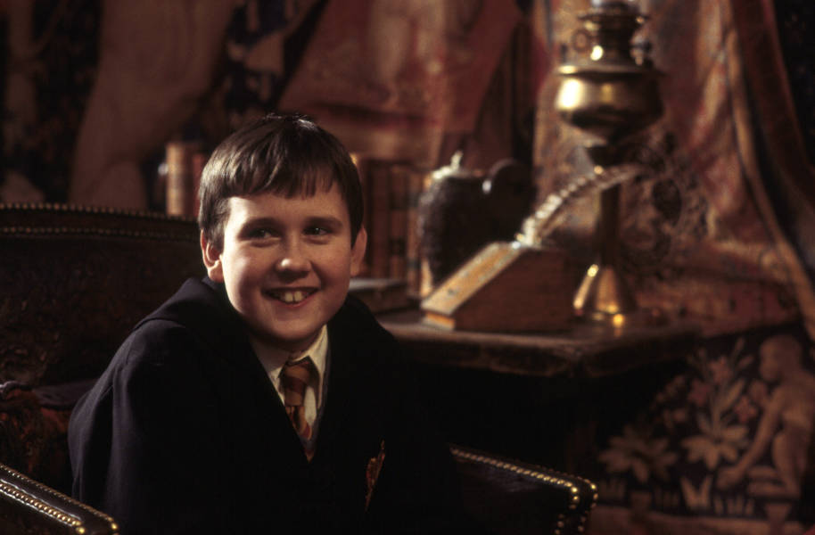Neville Longbottom is sitting in a chair and smiling