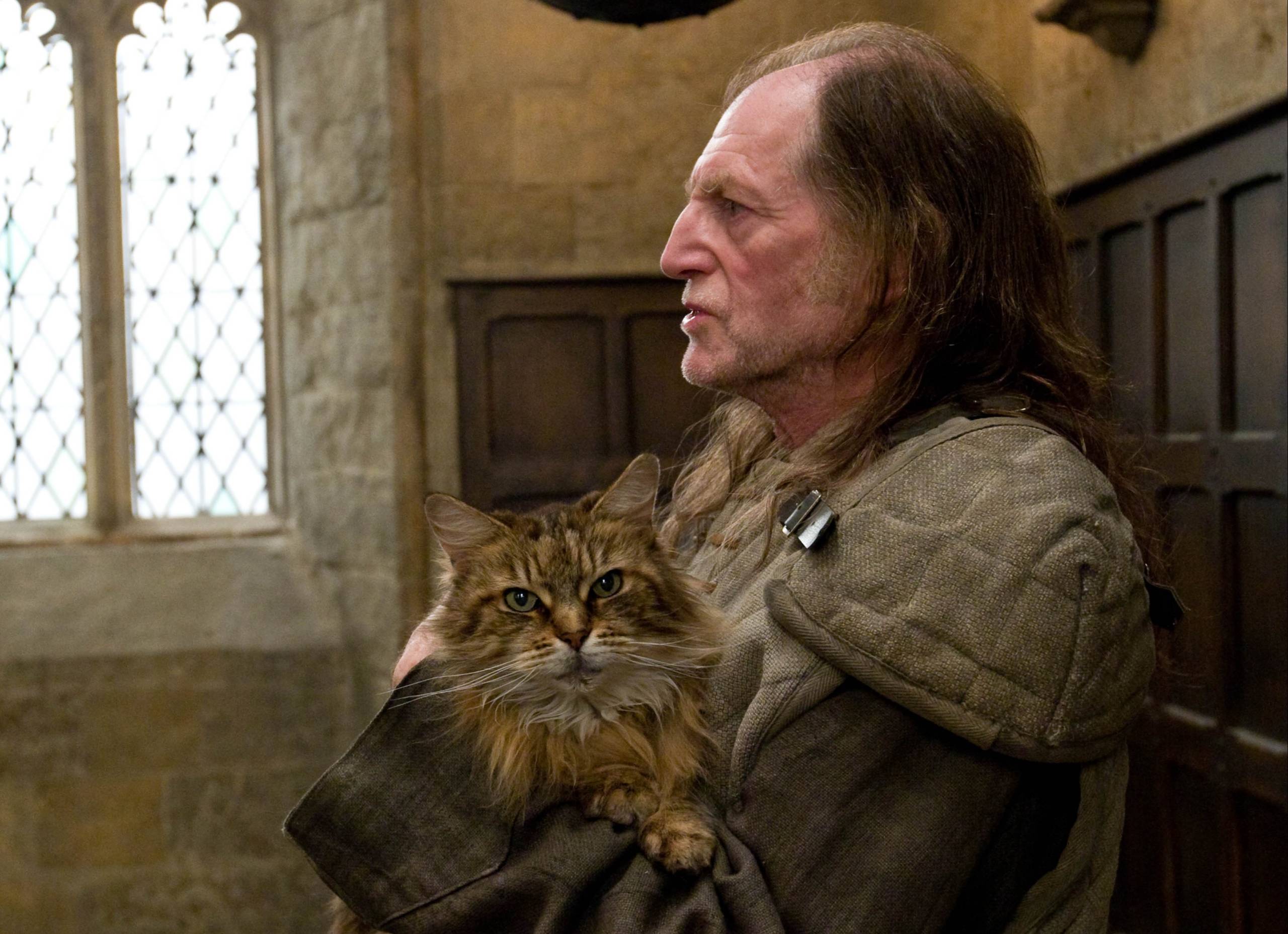 Argus Filch holding Mrs Norris patrolling Hogwarts corridors