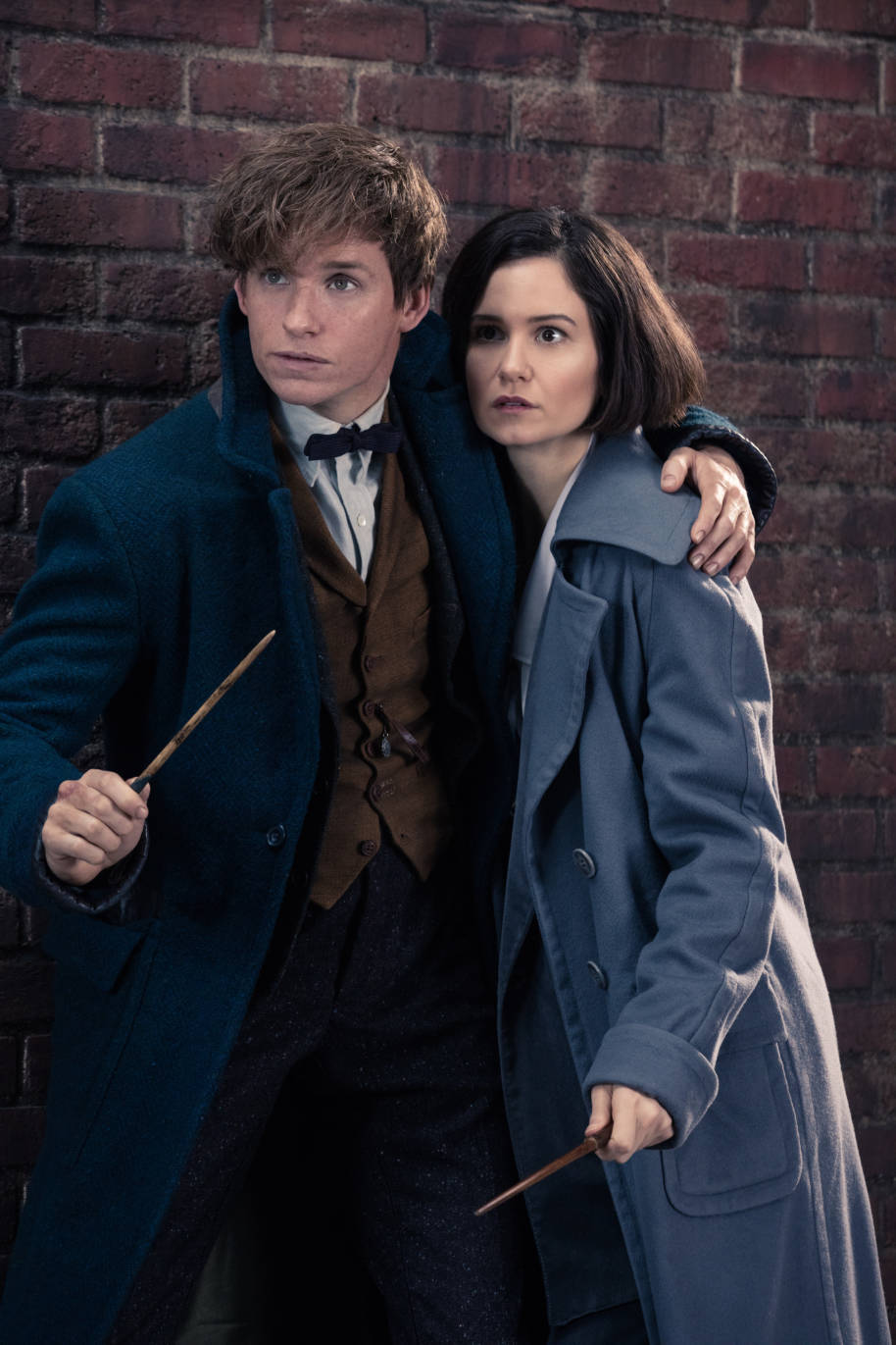 Newt Scamander met son bras autour de Tina Goldstein alors qu'ils s'abritent anxieusement avec leurs baguettes prêtes