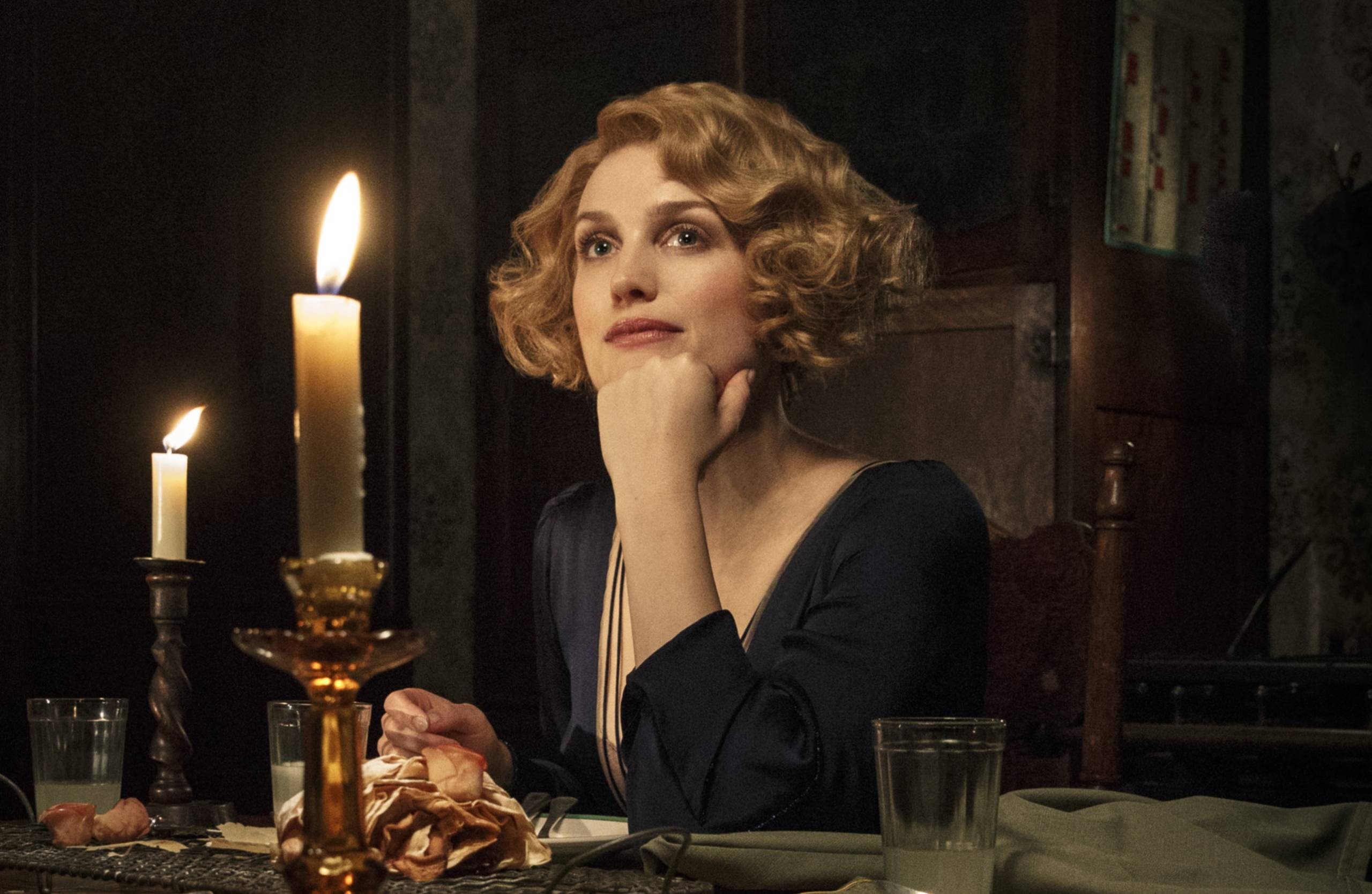 Queenie Goldstien rests her chin on her hand as she sits at a candlelit dinner table 