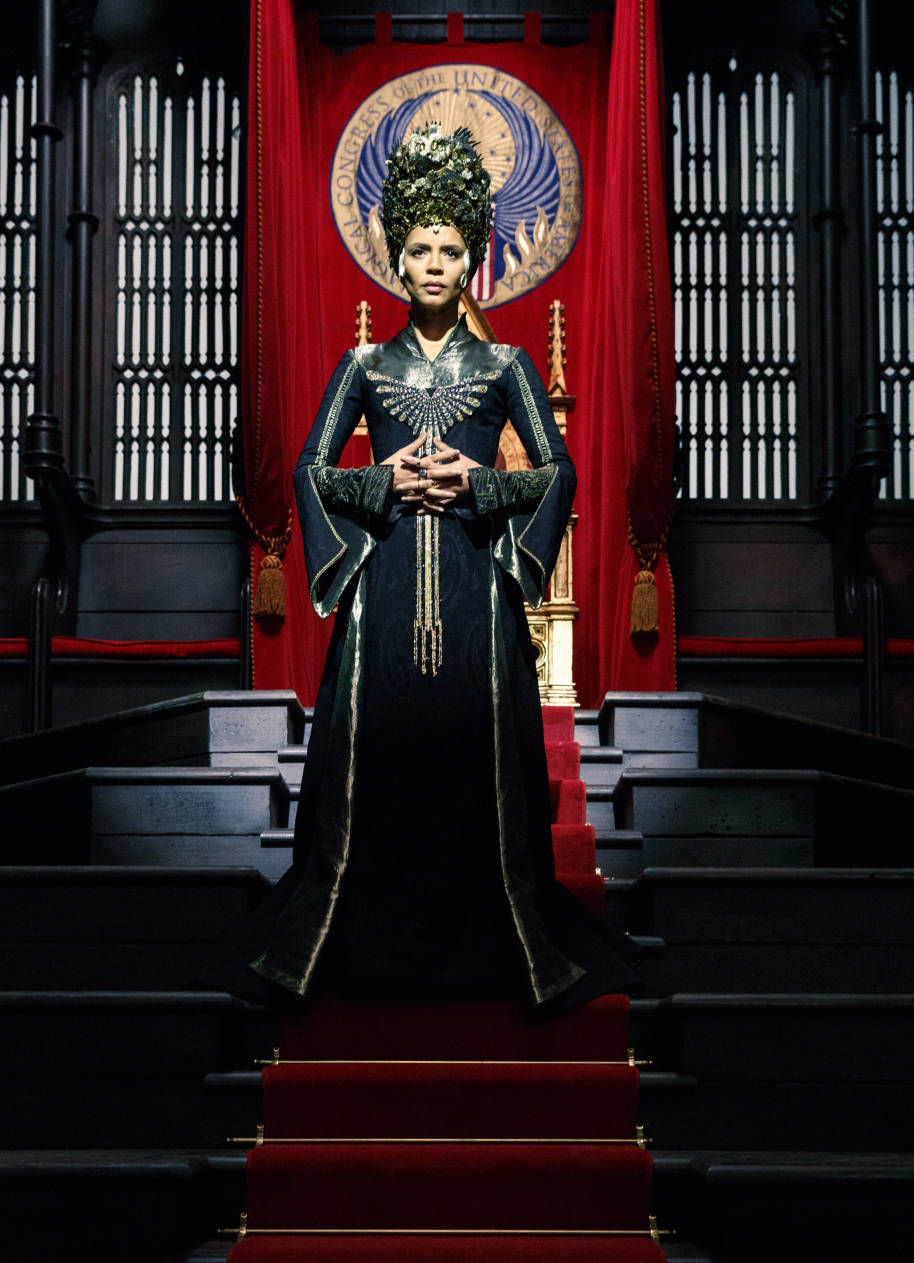 Seraphina Picquery the President of MACUSA stands in front of her President's Throne wearing black and gold robes and an impressive headdress 