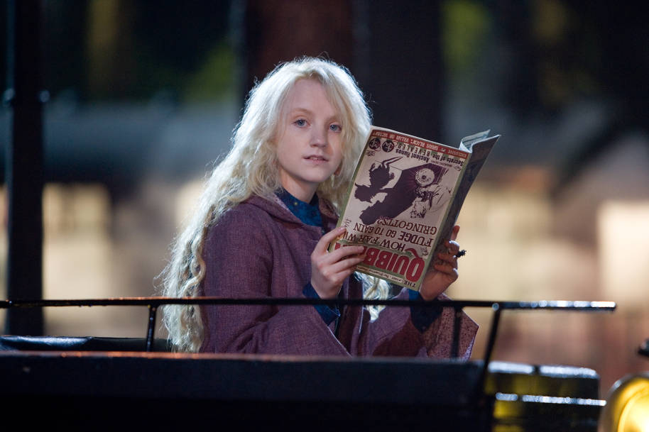 Luna sitting in a carriage holding The Quibbler upside down