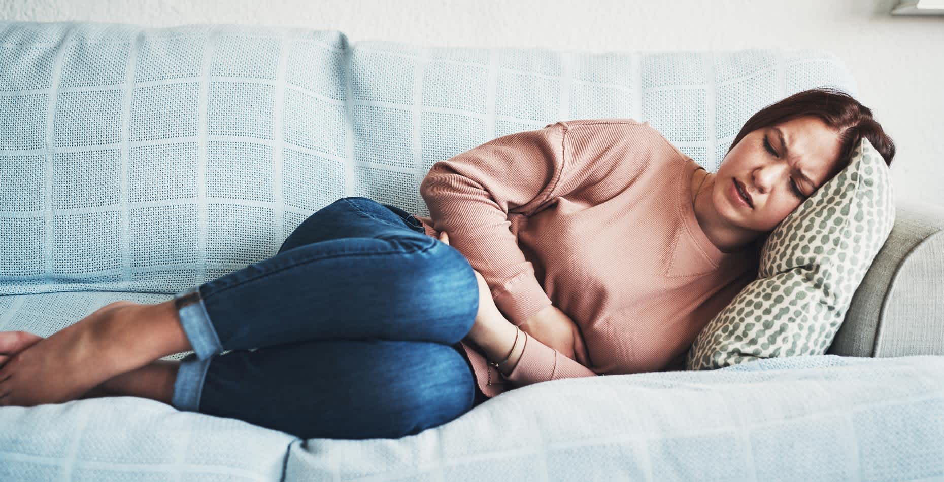 Young woman lying on couch due to stress affecting her digestive system