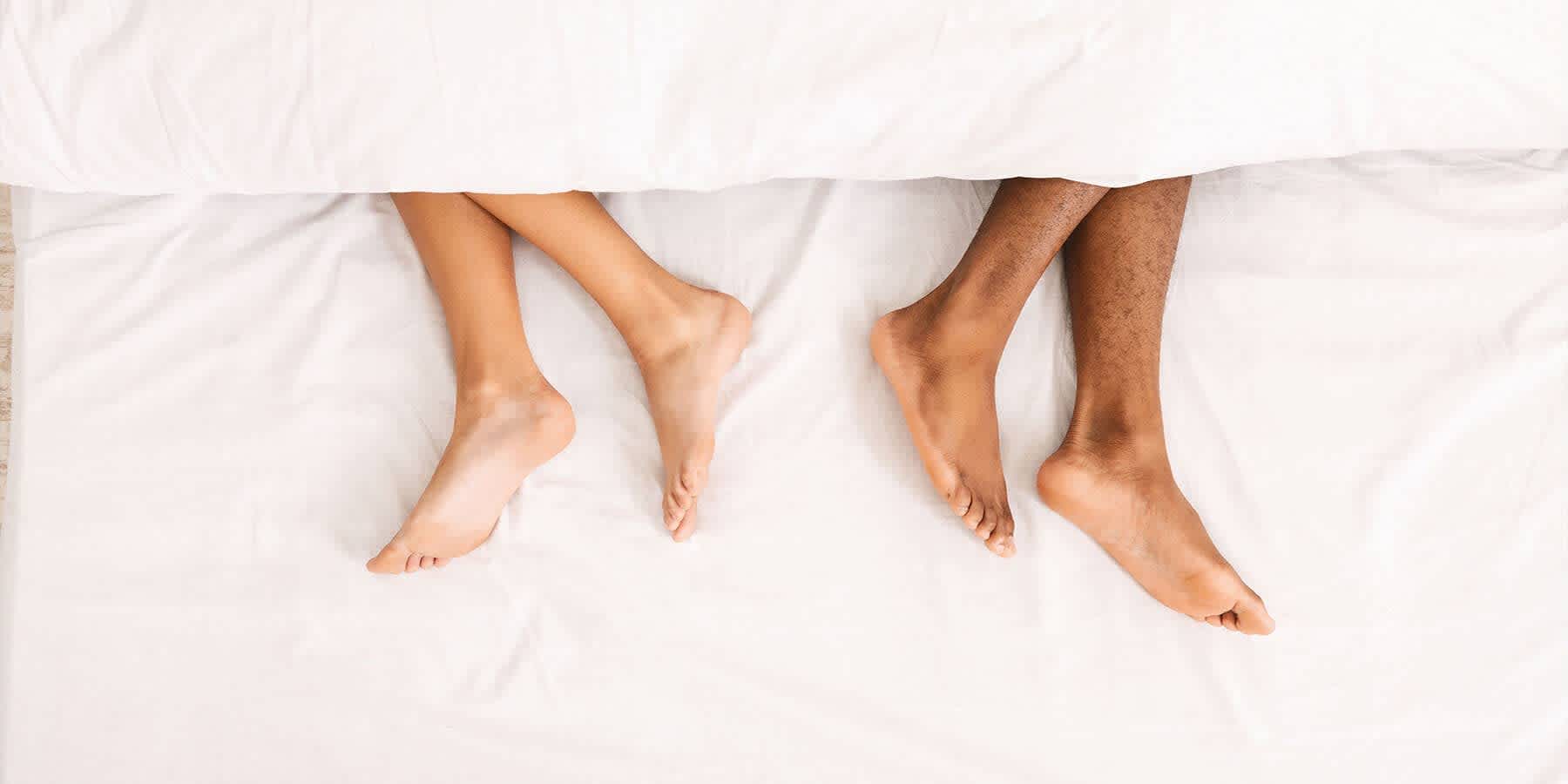 Couple lying in bed with feet facing away from each other while wondering about symptoms of HPV in males