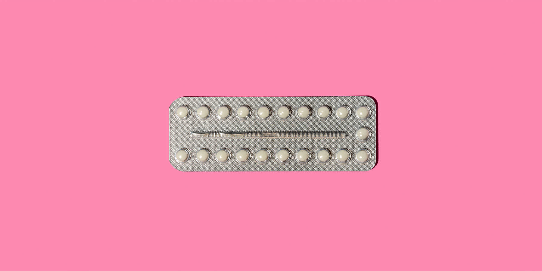 Birth control packet against a pink background
