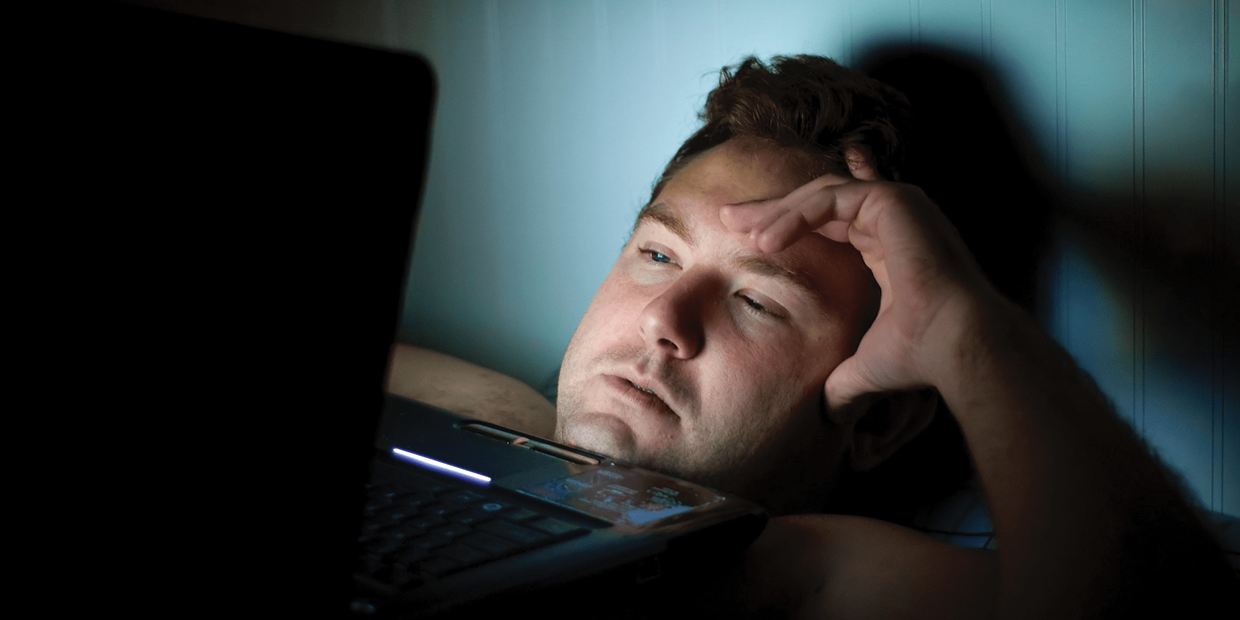 Man staying up late at night while using laptop to research if lack of sleep causes weight gain