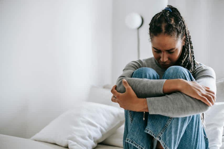 Woman sitting on bed holding knees in pain