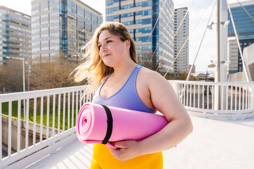 woman in bright clothing walking in a city with a yoga mat
