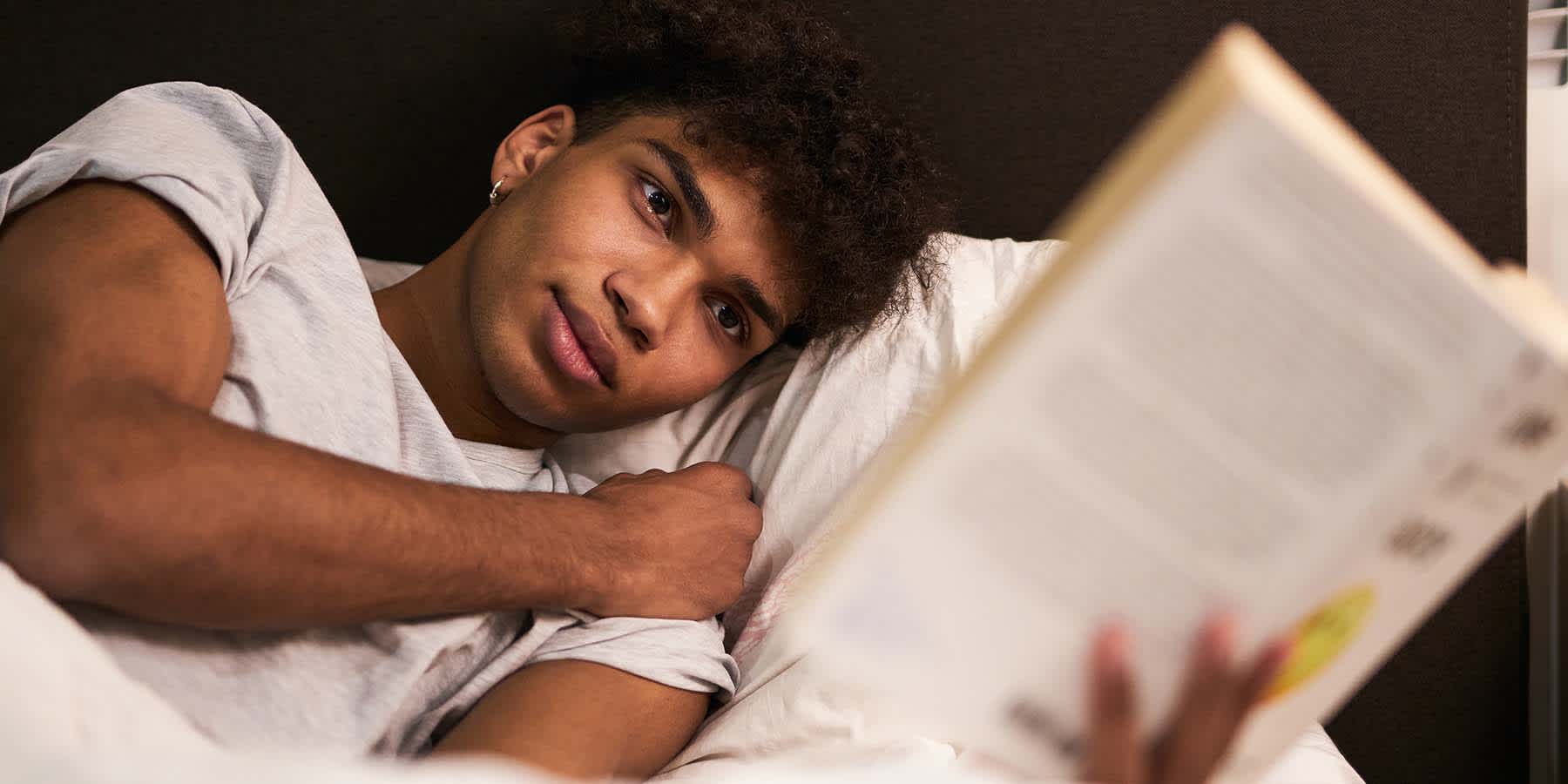 Young man with melatonin deficiency unable to sleep and reading a book in bed