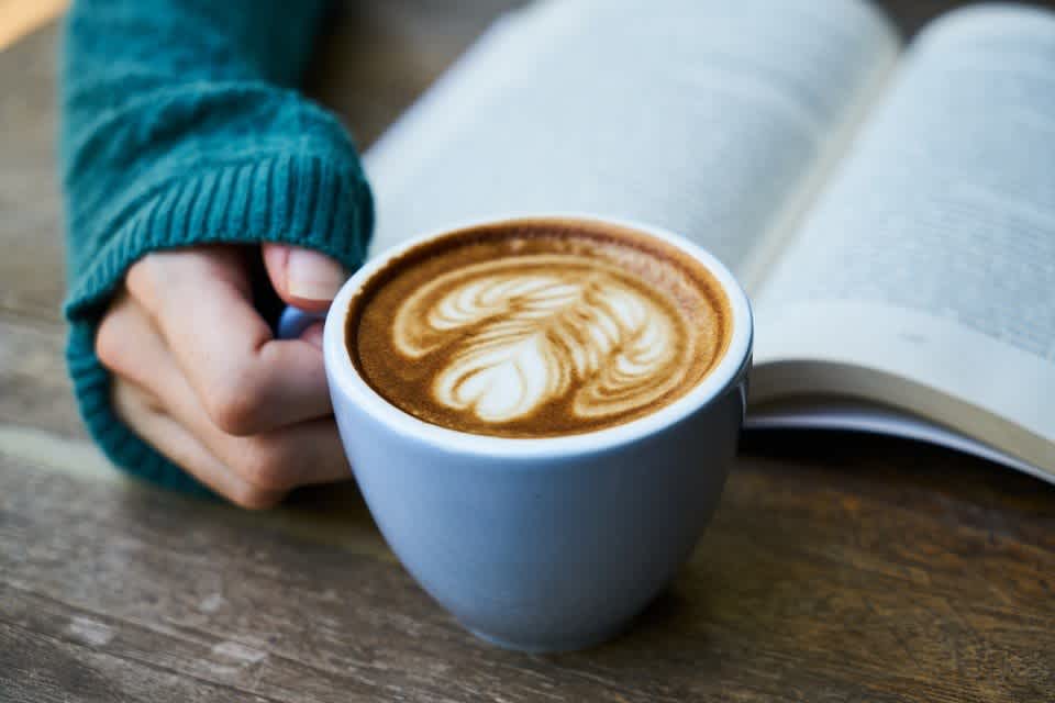 Woman drinking a coffee and reading about coffee for weight loss.