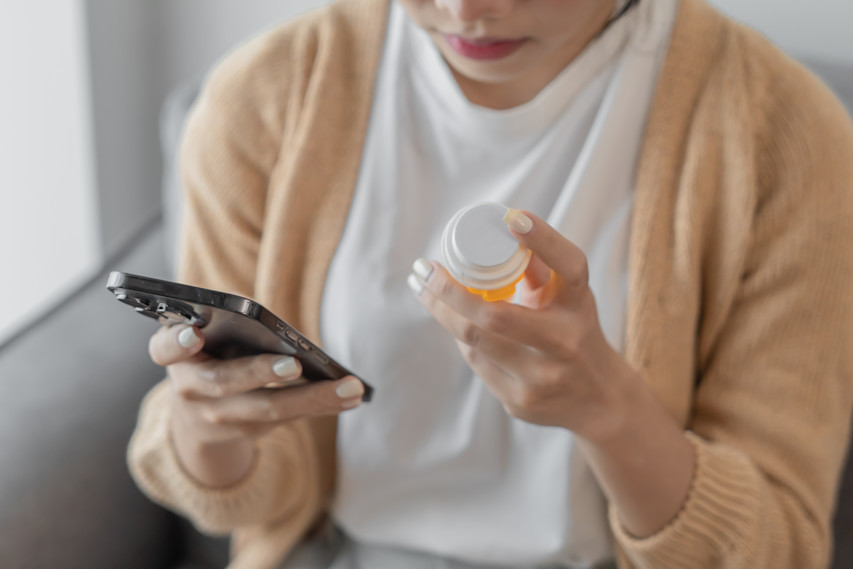 woman looking at phone and Rx bottle