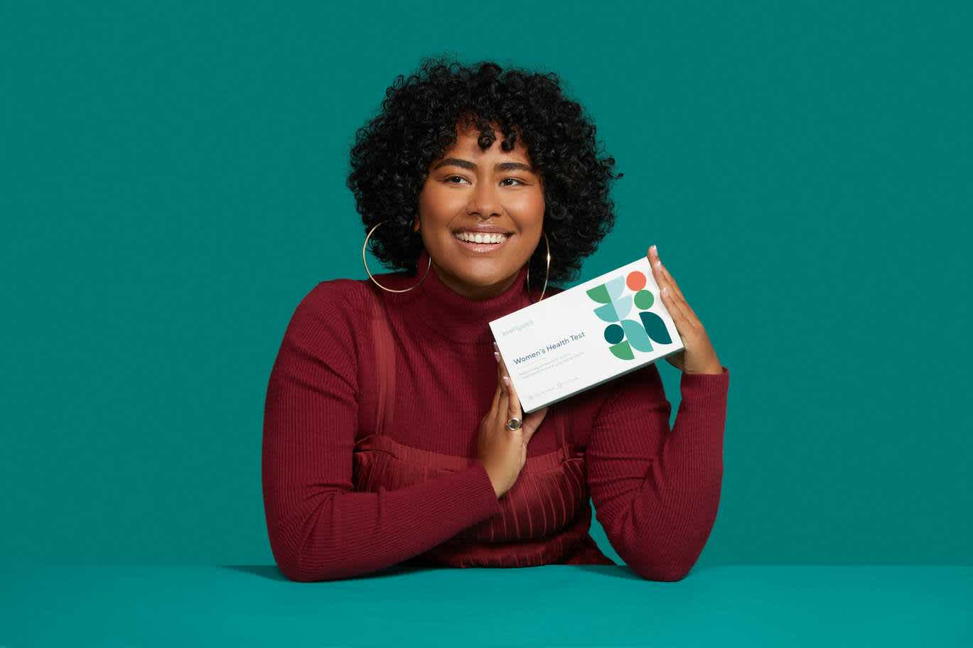 Woman smiling while holding Everlywell Women's Health Test