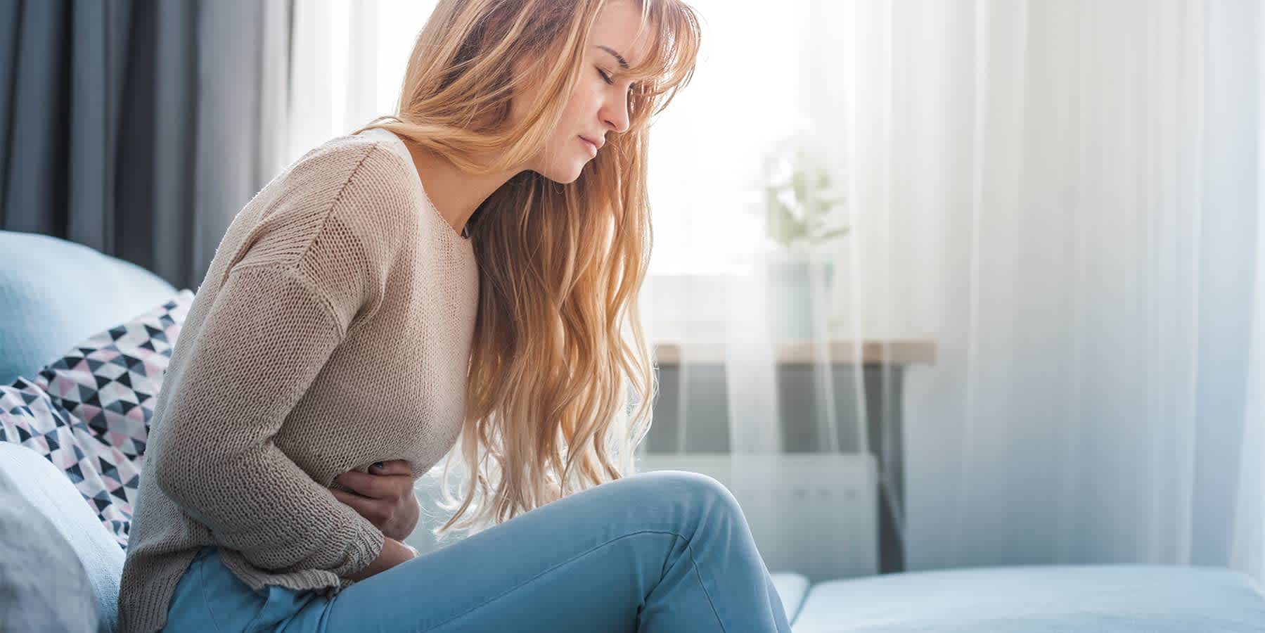 Woman sitting up on bed and experiencing digestive discomfort while wondering how long indigestion lasts