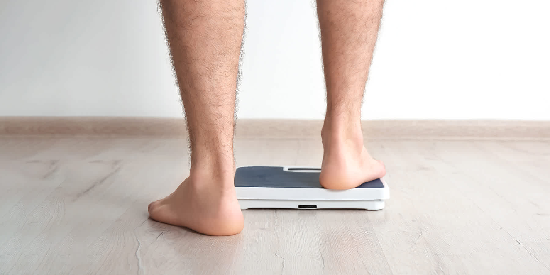 Man stepping onto bathroom scale while wondering about fat loss vs. weight loss