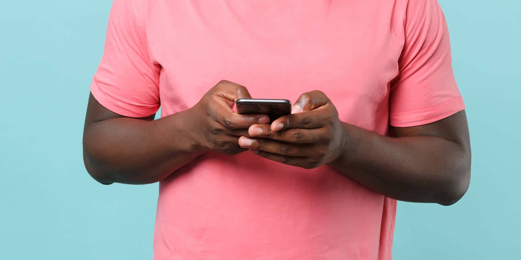 Man wearing pink shirt against a light blue background using mobile phone to look up syphilis tongue