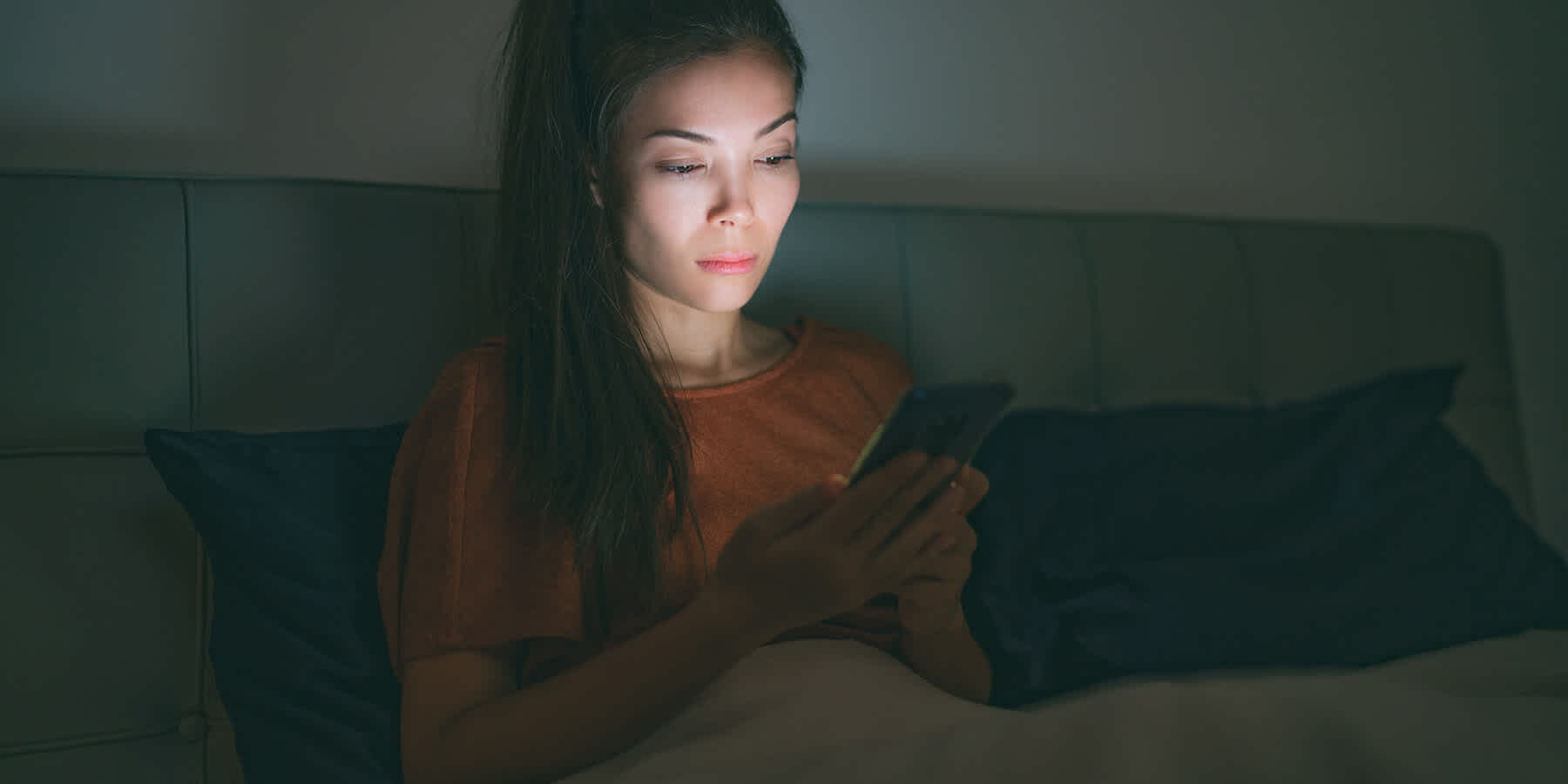 Woman sitting on bed with mobile phone and looking up how to handle stress-induced insomnia