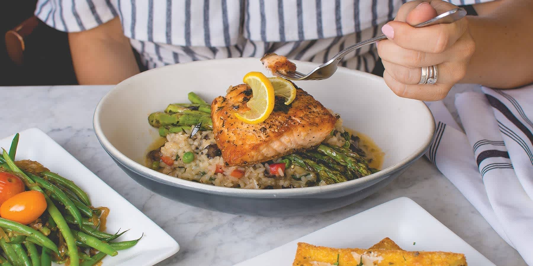 Salmon sitting on top of asparagus and rice in a white bowl