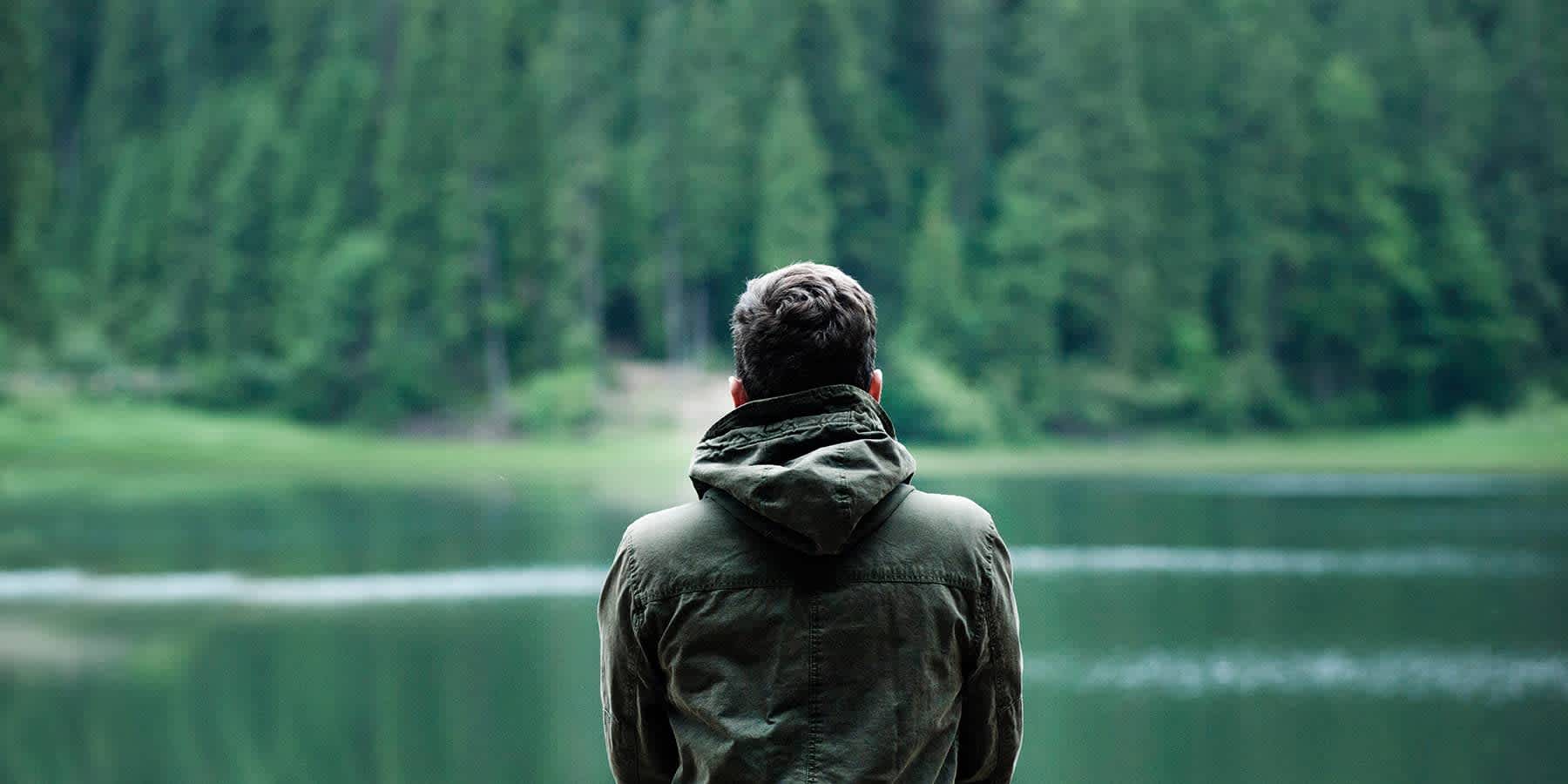 Man in jacket experiencing mood change while looking across lake and forest