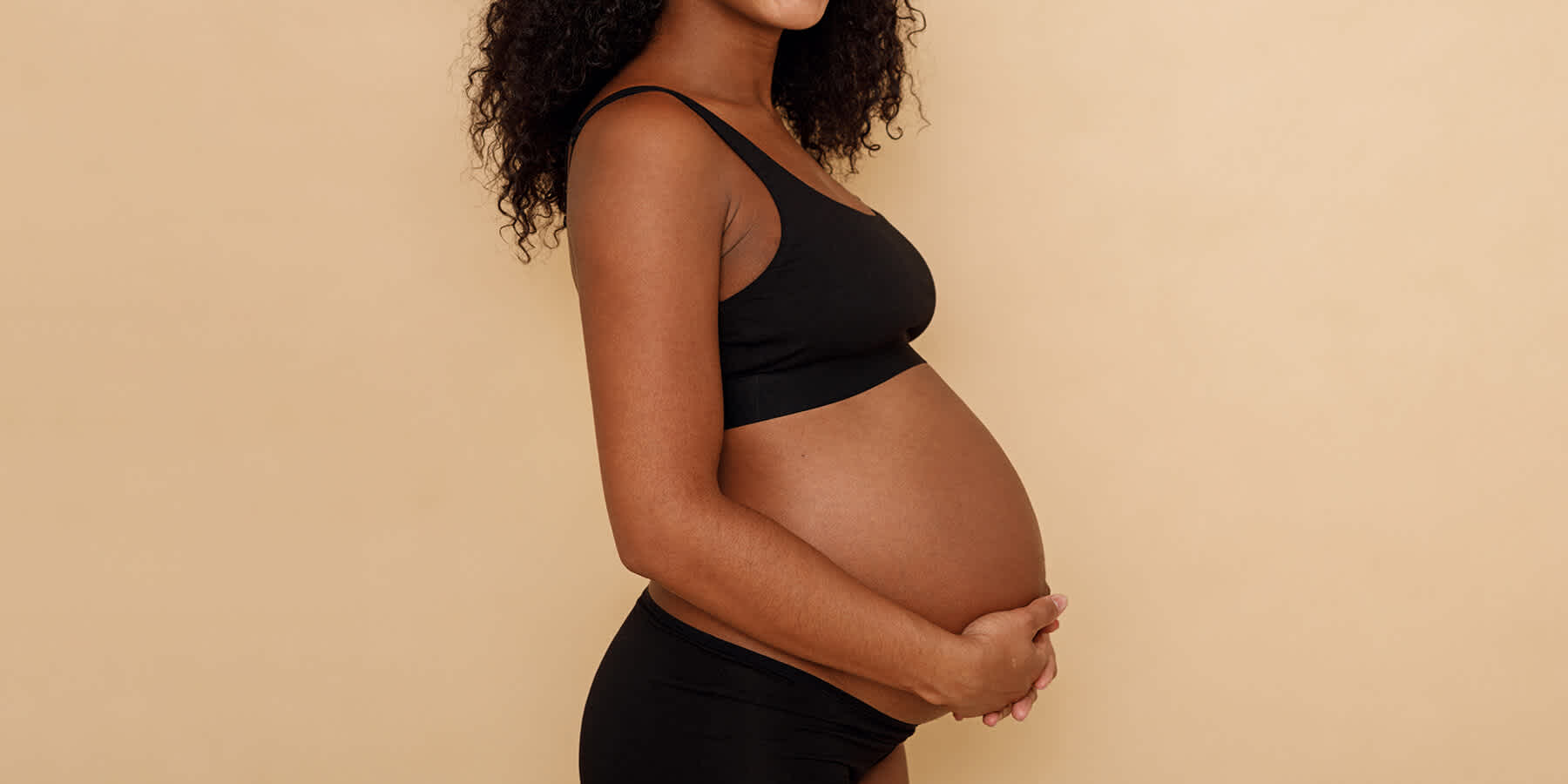 Pregnant woman holding belly against yellow background