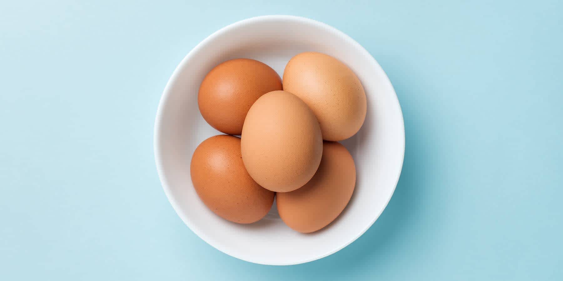 White bowl filled with eggs against a blue background