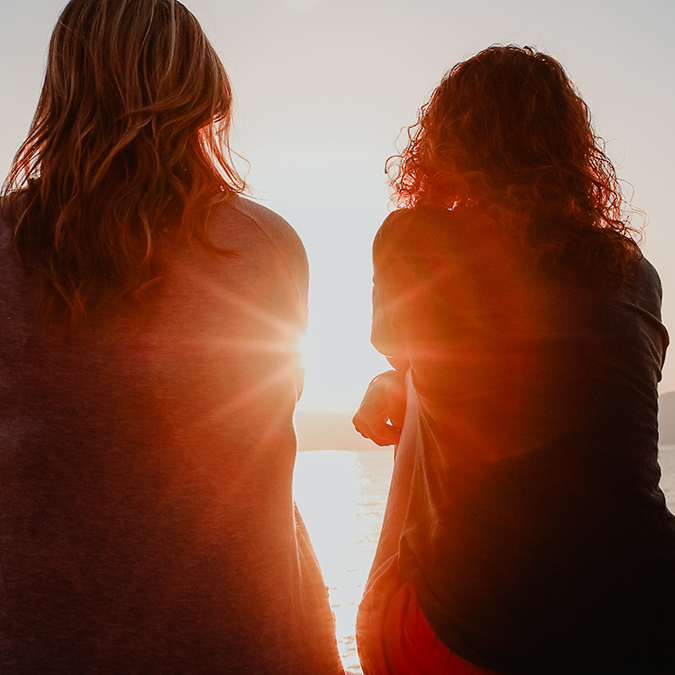 Two women looking at sunset while discussing HPV