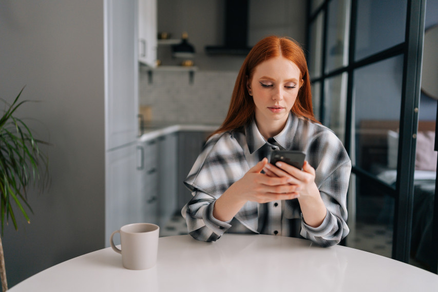 woman sitting at kitchen table with phone and coffee mug