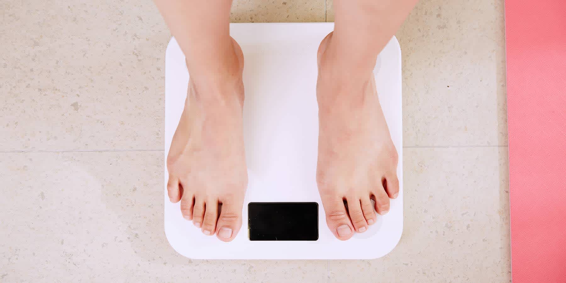 Woman standing on bathroom scale while wondering about weight fluctuation in women