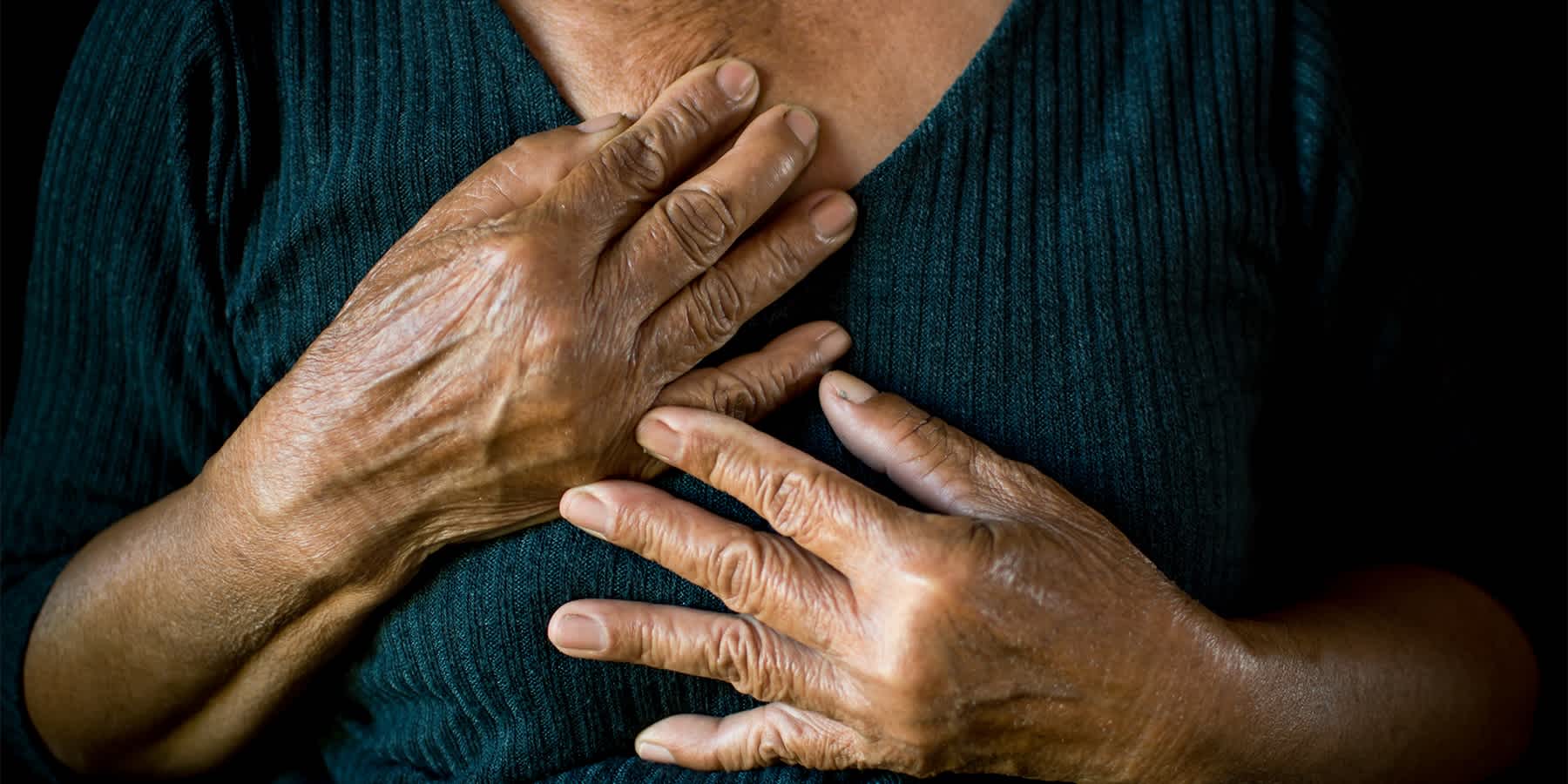 Elderly woman clasping her heart to symbolize coronary heart disease