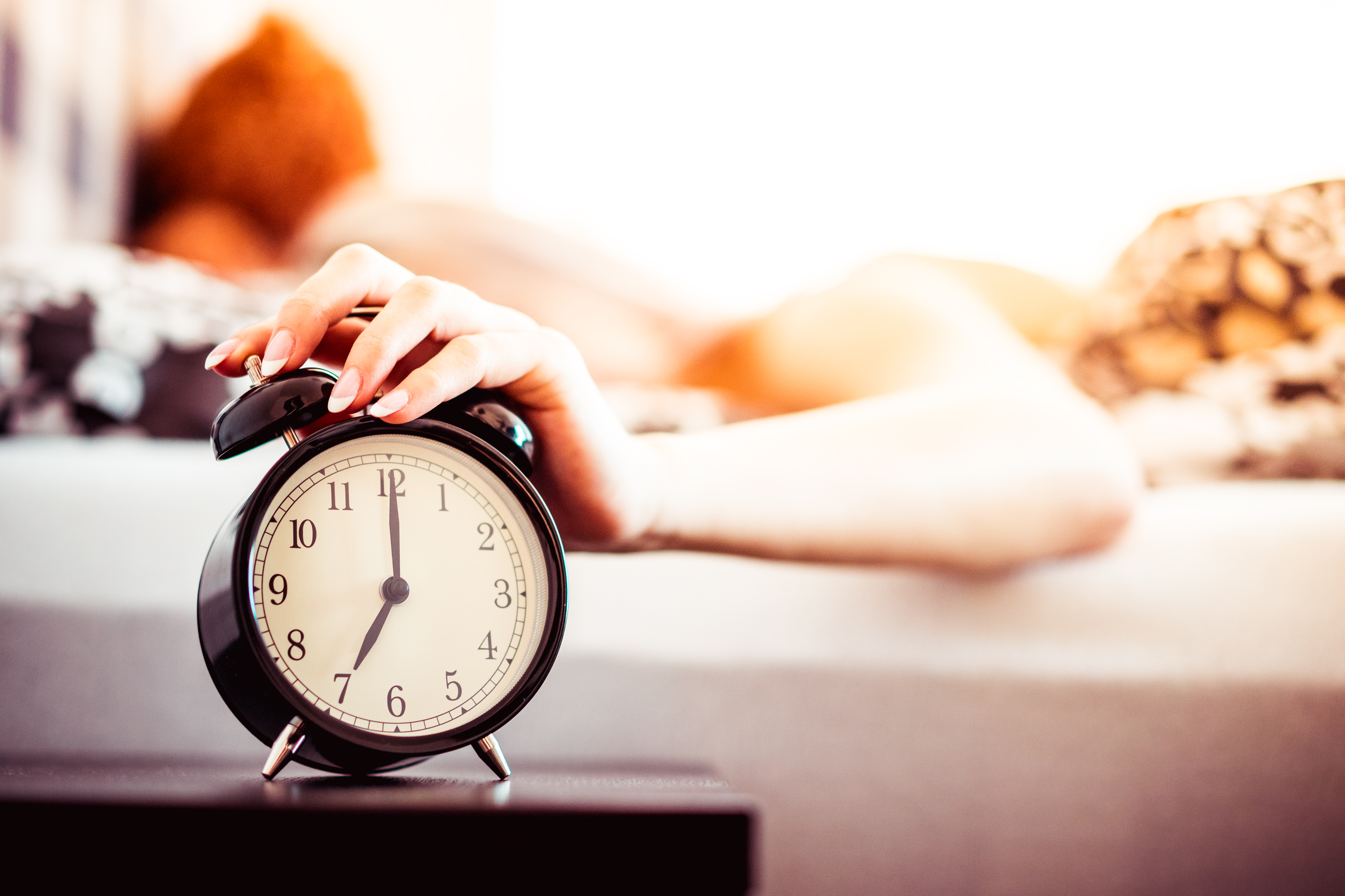 woman-shutting-off-ringing-alarm-clock-from-bed-picjumbo-com