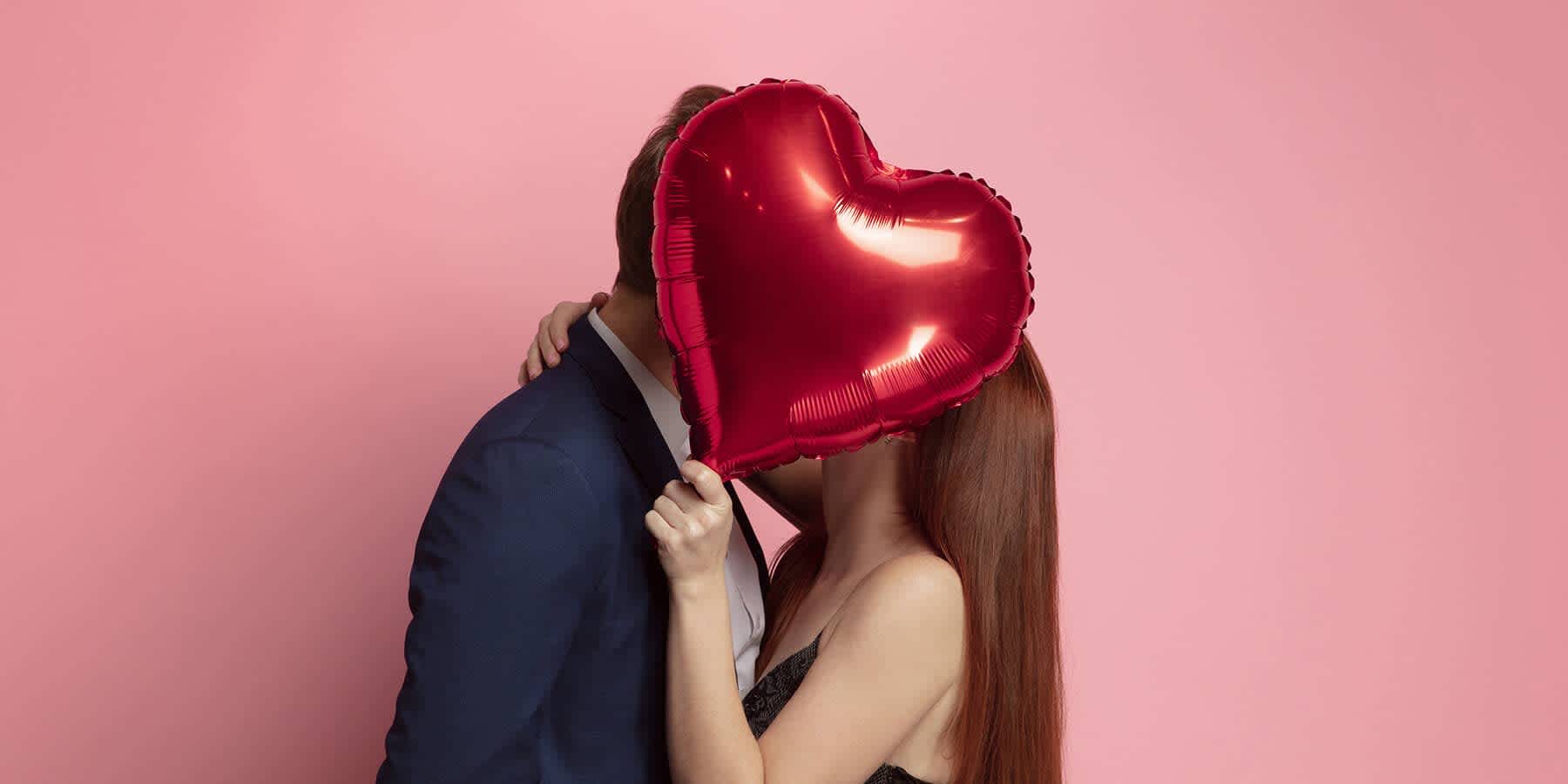 Young couple holding valentine-shaped balloon while kissing after using safe sex practices to avoid STDs