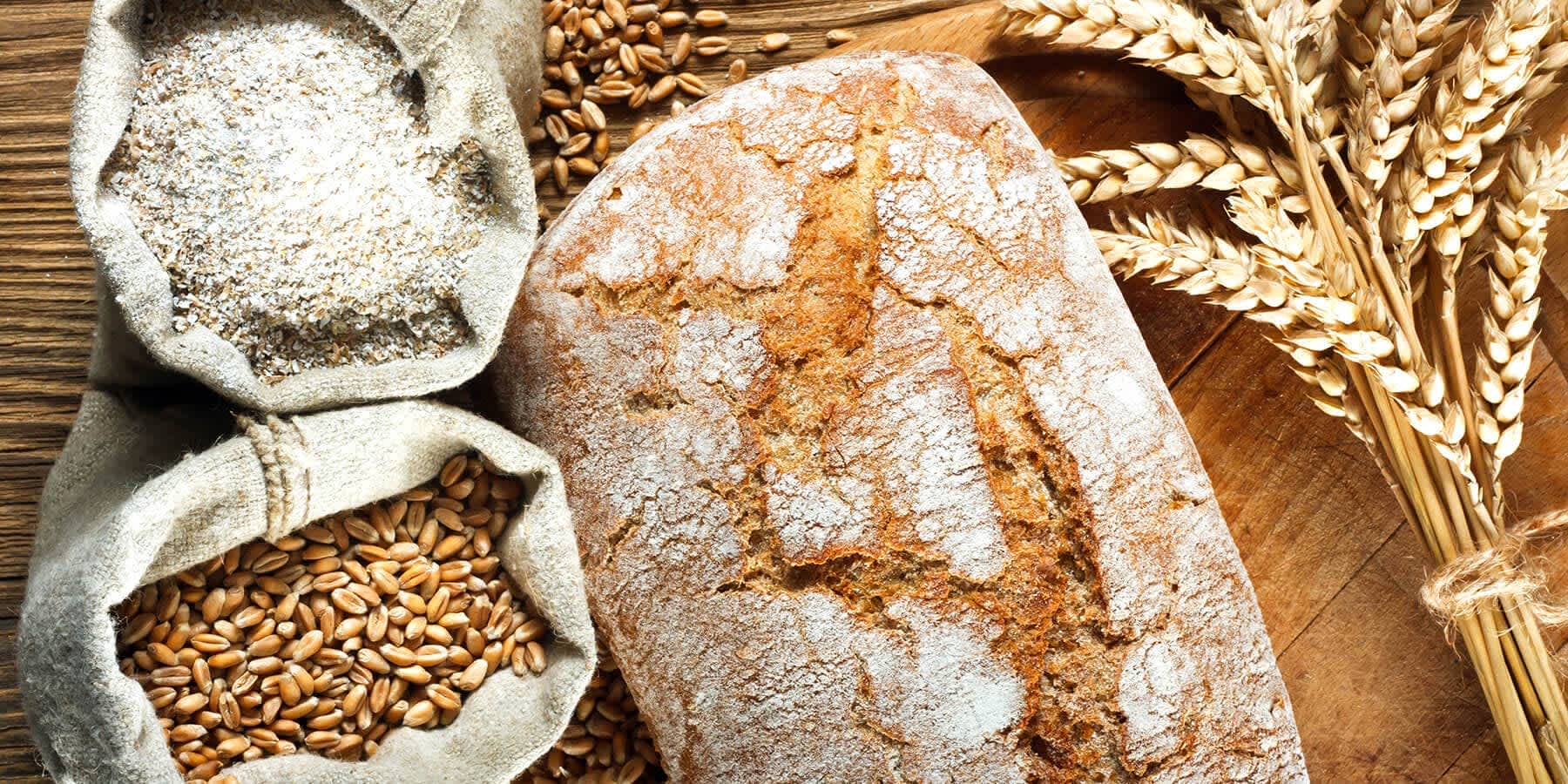 A loaf of bread next to a variety of grains on a table