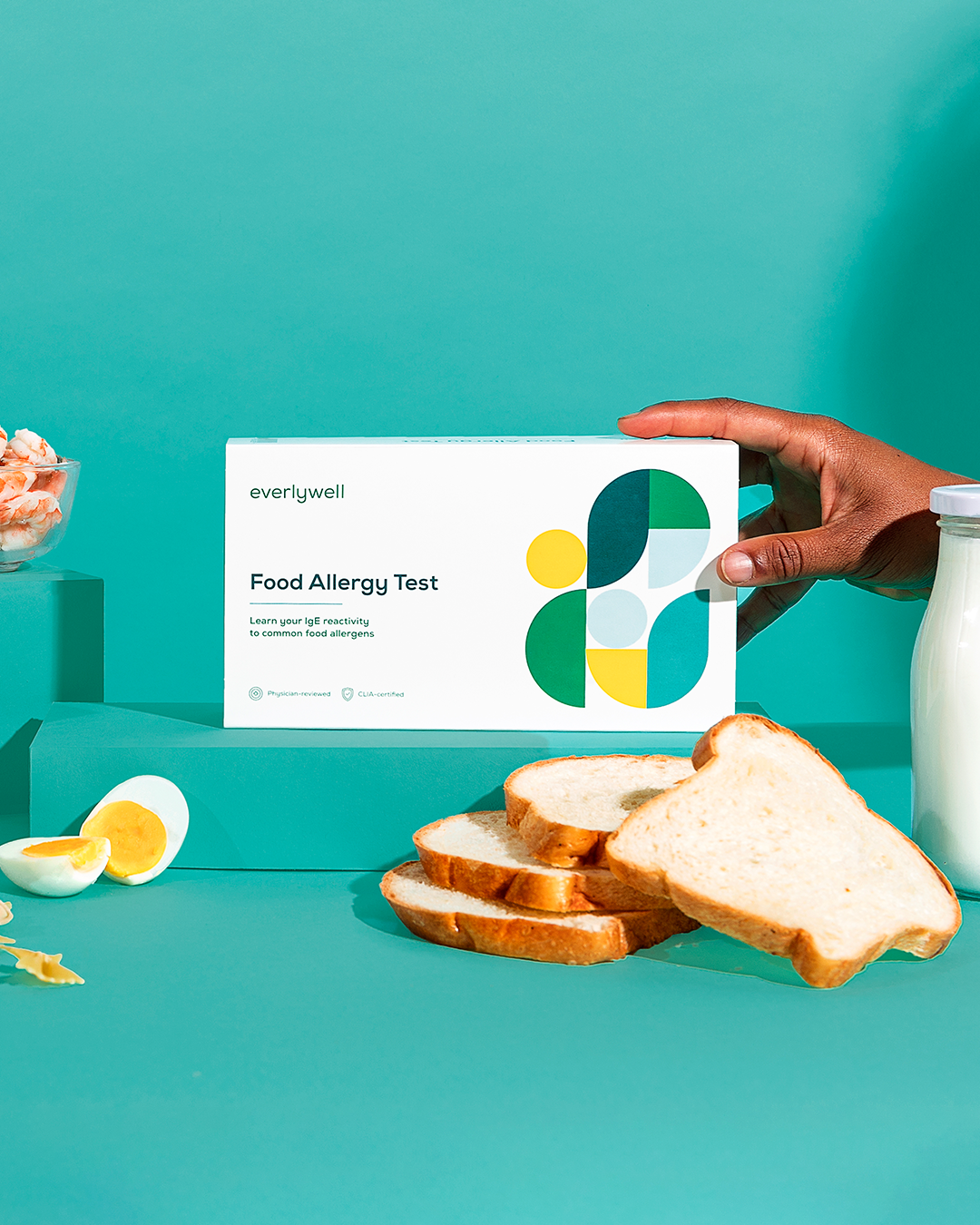Everlywell food allergy test surrounded by common food allergens against blue background