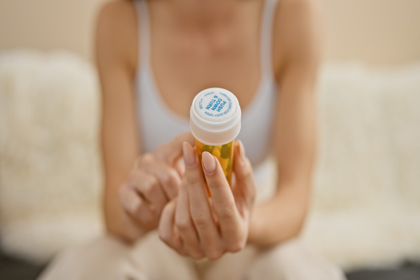 woman blurred in background holding up and reading pill bottle