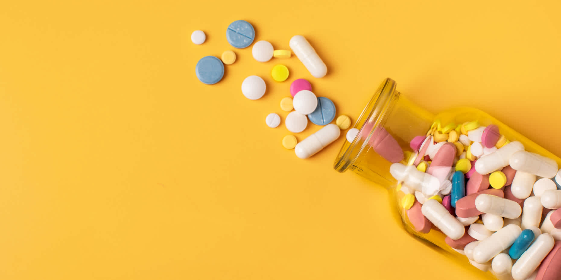 Open bottle of expired multivitamins against a yellow background