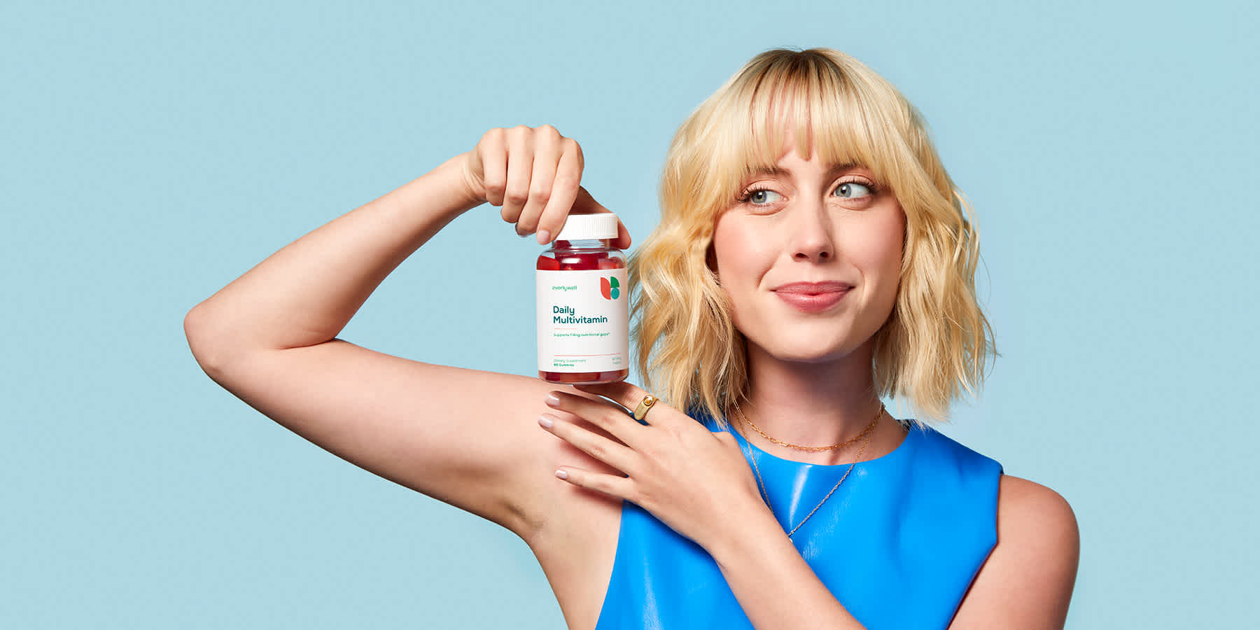 Young woman holding bottle of Everlywell Daily Multivitamins against a blue background